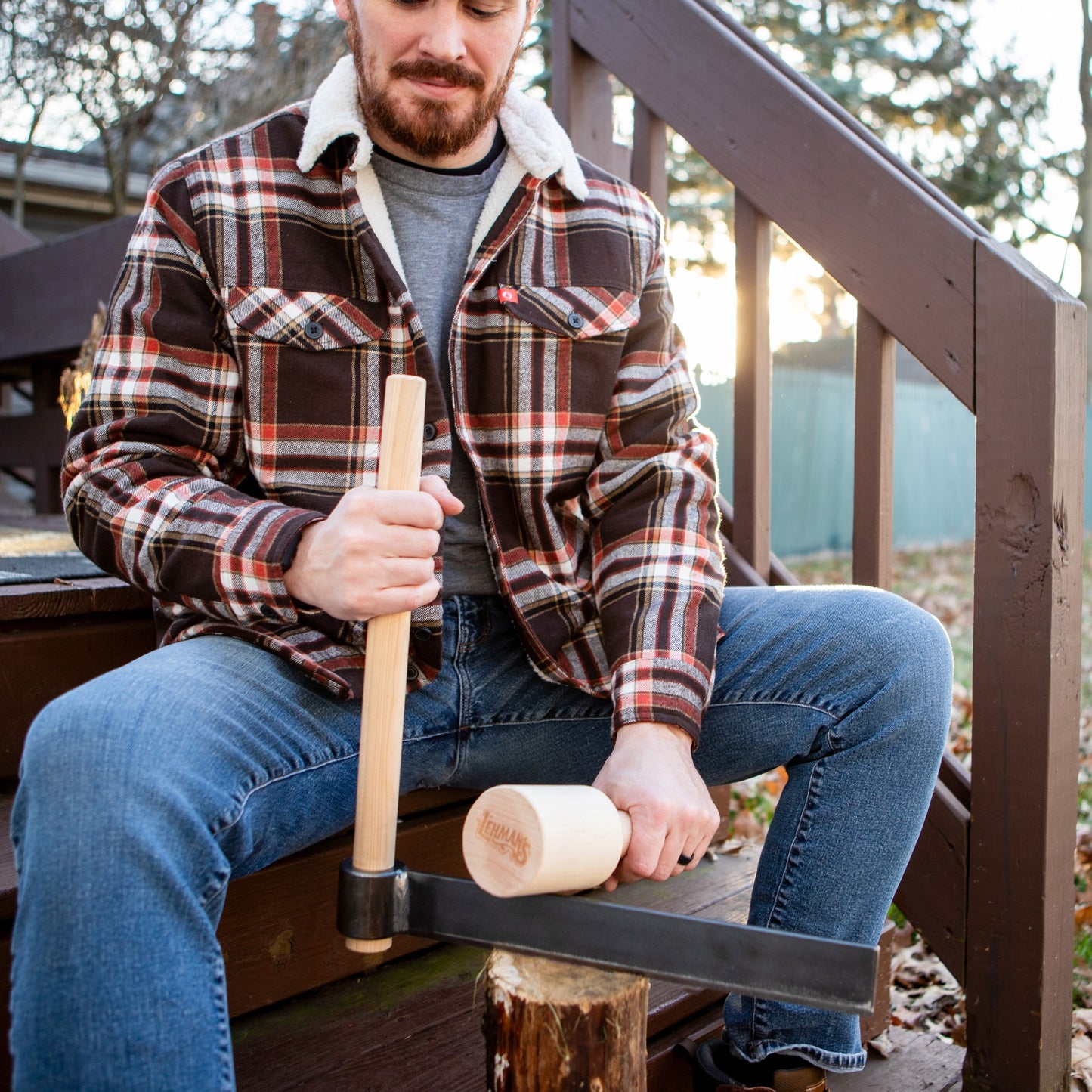 Man wearing a plaid jacket and jeans demonstrating use of a handcrafted Amish made wood splitting froe and birch mallet set for kindling, part of Farm, Garden & Tool and USA Made collections.