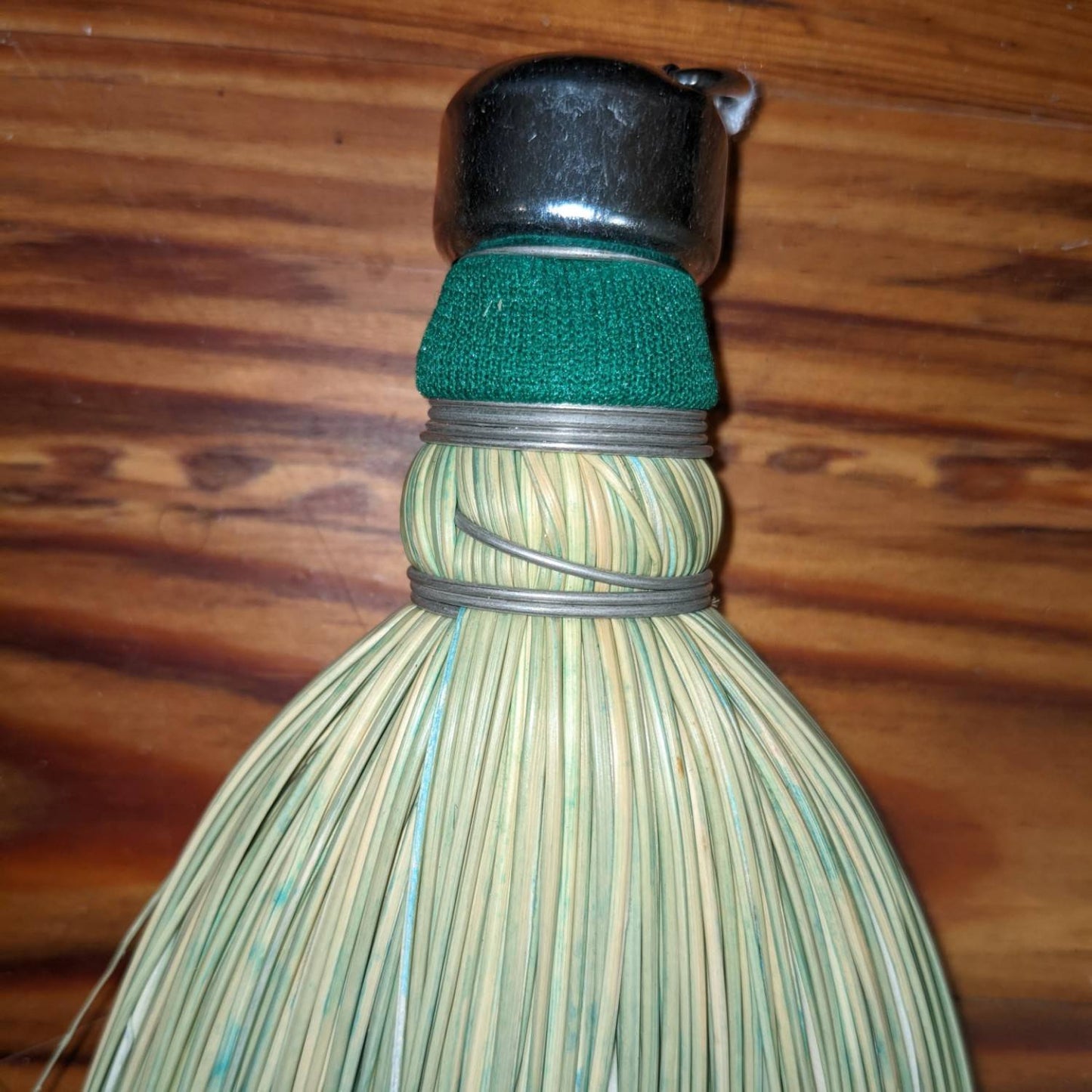 Handcrafted corn whisk broom made in the USA with tightly bound natural corn straw, featuring a metal cap and green fabric band, ideal for household cleaning tasks.