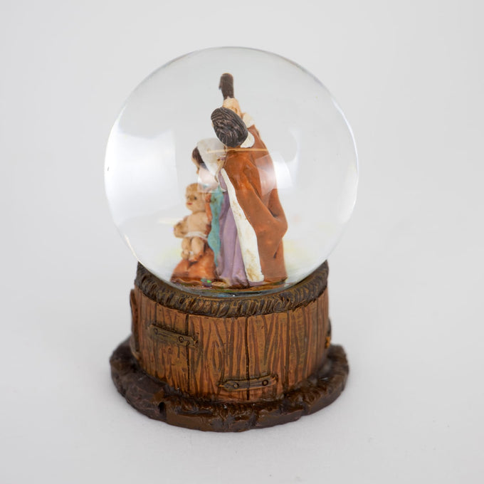 Miniature handcrafted snow globe featuring hand-painted figurines of the Holy Family inside a clear glass dome with a detailed wood-textured base, ideal for holiday decor collections.