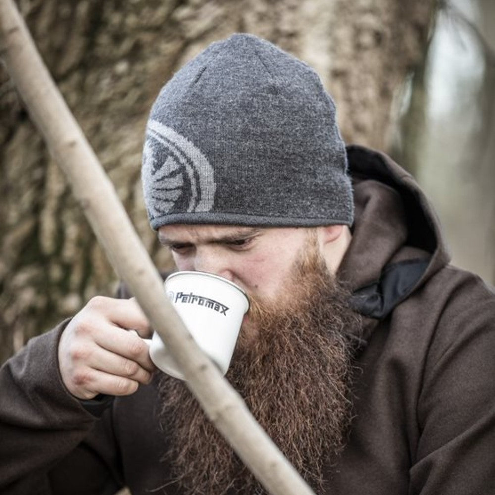 Bearded man wearing a gray knit hat and brown hoodie sipping from a white Petromax enamel mug outdoors, suitable for Farm, Garden & Tool, Camping, Brewing Coffee and Tea, Kitchen & Food, Dinnerware, and Best Sellers collections.
