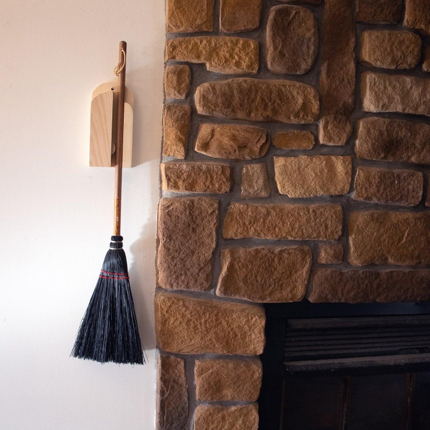 Handcrafted wooden wall rack holding a traditional broom beside a stone fireplace, showcasing Amish made quality and practical design for Home & Decor and Household Helpers collections.