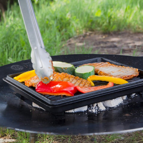 Square cast iron grill pan cooking seasoned pork chops and colorful bell peppers over glowing charcoal outdoors, ideal for farm, garden, camping, kitchen, cookware, and cast iron collections.