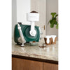 Green stand mixer equipped with a white grain mill attachment grinding coffee beans on a kitchen countertop, surrounded by coffee cups and a bowl, for Kitchen & Food, Baking Supplies, and Grain Mills collections.