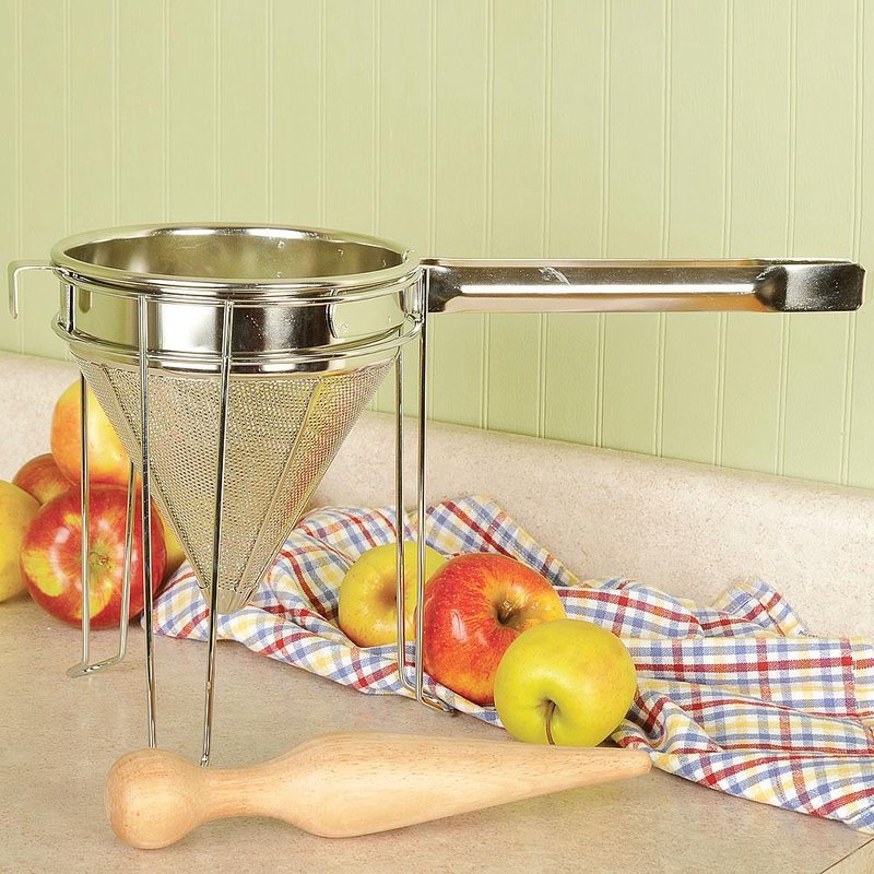 Sturdy stainless steel food mill with a conical mesh basket and rolled edge handle, shown with a wooden plunger and fresh apples, ideal for Kitchen & Food and Food Prep collections.