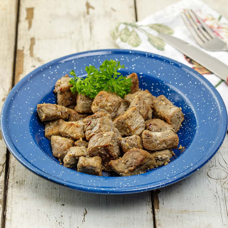 Blue enamel dish filled with seasoned freeze-dried hand-cut beef cubes garnished with fresh parsley, showcased on rustic wooden table in Kitchen & Food, Freeze Dried, USA Made collections.