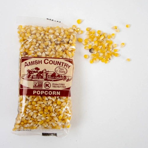 Clear bag of handcrafted Amish Country yellow popcorn kernels with some kernels spilled beside it on a white surface, featured in Kitchen & Food, Snacks and Sweets, Popcorn, and USA Made collections.