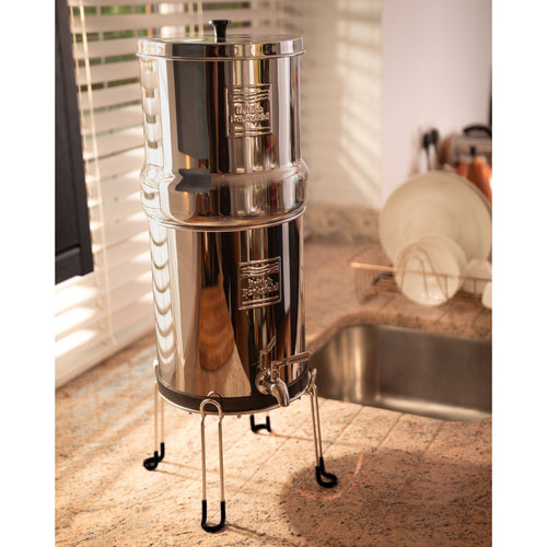 Polished stainless steel gravity water filter set elevated on a handcrafted sturdy stand with protective feet, designed for convenient dispensing in Appliances, Emergency Supplies, and Water Heating and Treatment collections.