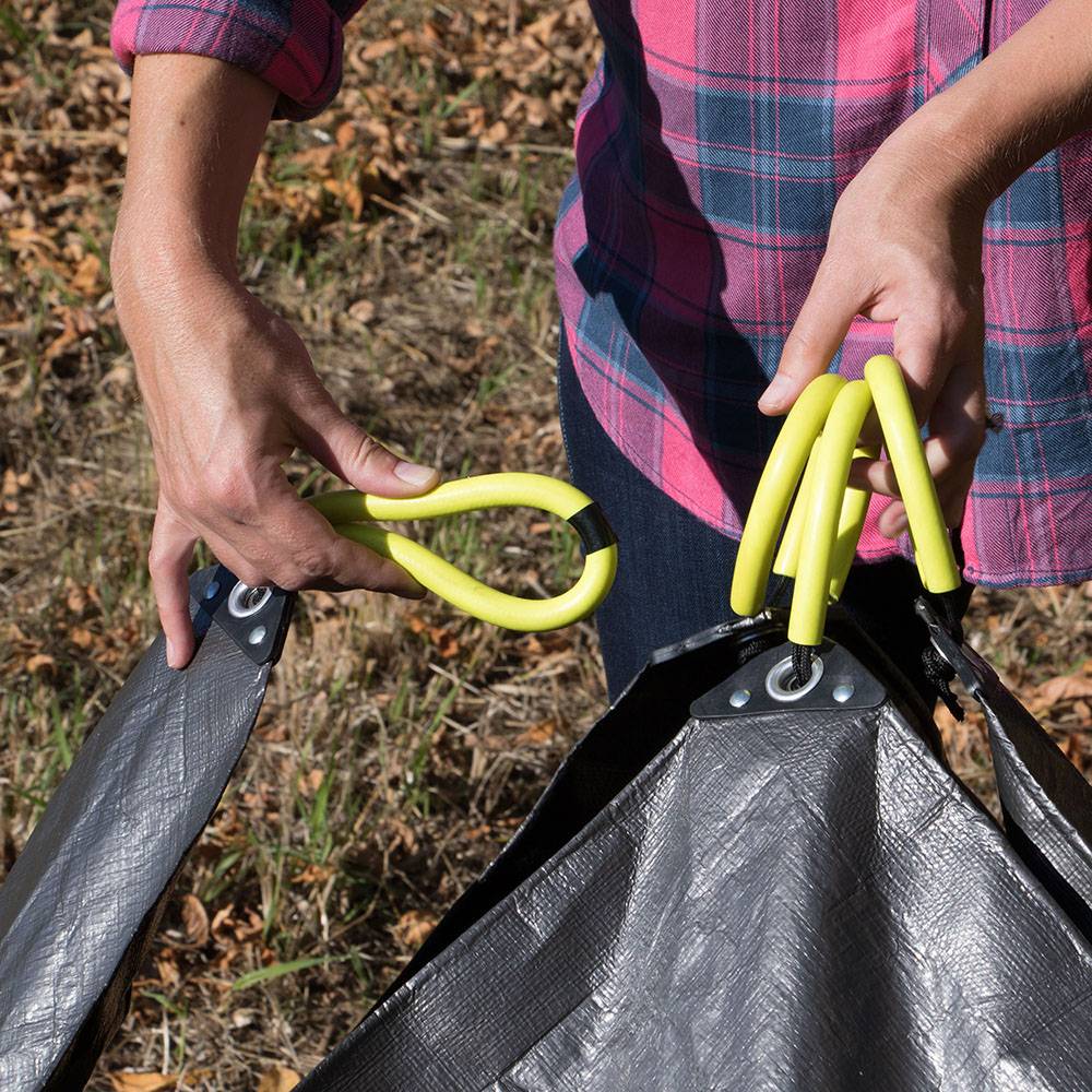Person interlocking four bright yellow soft grip rubber handles attached to a dark woven polyethylene tarp outdoors for easy yard cleanup in Farm, Garden & Tool and Lawncare collections.