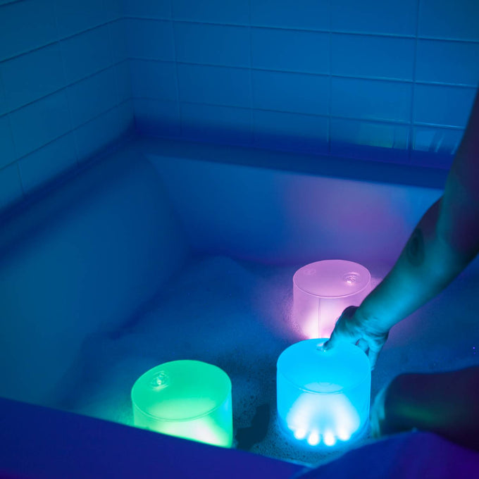 Three glowing inflatable solar LED lights in blue, green, and soft purple hues floating in a bathtub filled with bubbles, showcasing their waterproof, portable design for camping, emergency supplies, and outdoor lighting.