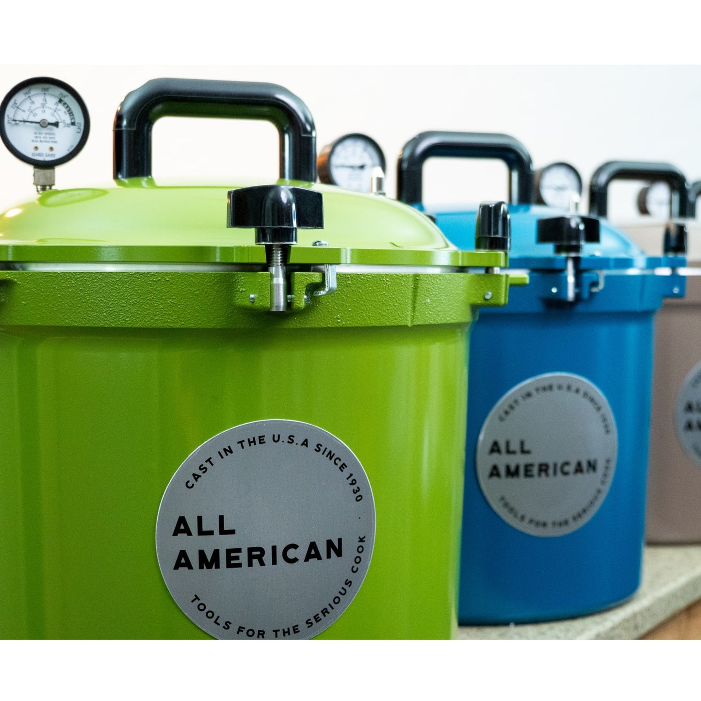 Row of colorful pressure canners featuring sturdy handles and pressure gauges, made in USA for food preservation, canning, and kitchen collections, highlighting durable design.