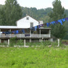 Long clothesline stretched between trees and posts in a rural setting, holding various dark-colored garments drying outdoors, reflecting a simple laundry setup in a natural home environment.