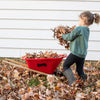 Child playing outdoors with a red handcrafted kids wheelbarrow by Lehman’s, helping collect autumn leaves, in a yard setting promoting outdoor play and garden fun collections.