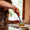 Person using a red lighter to ignite wick element submerged in olive oil inside a small clear glass jar, highlighting a USA made olive oil lamp kit for lamps and lighting collections.