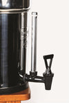 Close-up of a stainless steel and black plastic water spigot with a clear sight glass tube attached to a polished metal water filter, ideal for water heating and treatment in appliance collections.