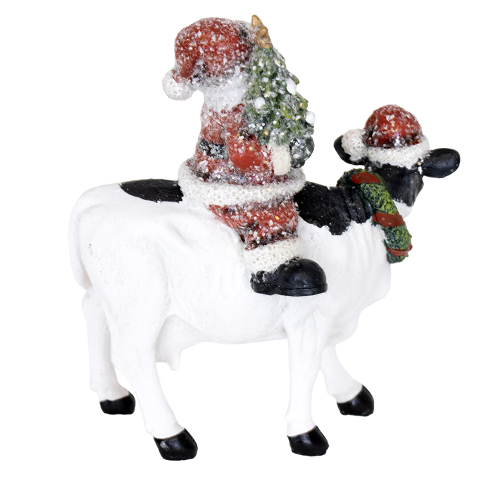 Handcrafted 6-inch resin figurine featuring Santa holding a Christmas tree while riding a black and white cow wearing a festive wreath and Santa hat, adding cozy country charm to Home & Decor, Holiday Decor, Best Sellers, and Promo Eligible collections.