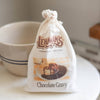 Lehman's Chocolate Gravy Mix packaged in a charming fabric bag, set on a white surface beside a beige bowl with blue stripes, ideal for Kitchen & Food, Snacks and Sweets, Pantry, Dry Goods and Mixes, Best Sellers, and Promo Eligible collections.