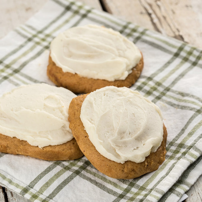 Three moist pumpkin cookies topped with creamy white frosting, displayed on a green and white plaid cloth, highlighting a handcrafted treat from Amish Country, perfect for Kitchen & Food and Snacks and Sweets collections.