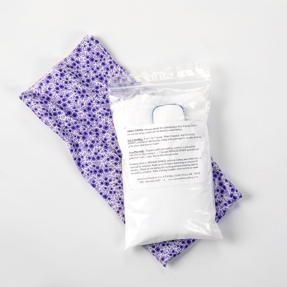 Clear plastic resealable bag filled with white fabric soak powder resting on a folded purple cloth with a floral pattern, featured in Home & Decor and Laundry Supplies collections.