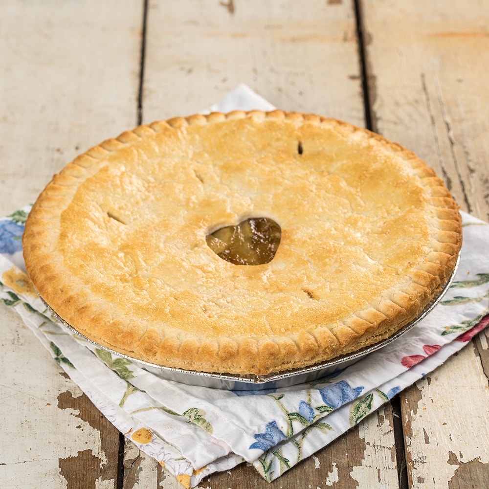 Golden brown homemade apple pie with a flaky crust resting on a floral cloth on rustic wooden table, handcrafted and made in USA, perfect for kitchen and food collections