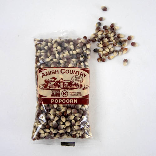 Clear plastic bag of handcrafted Amish Country popcorn kernels with a rich variegated brown and cream color, spilling onto a white background, featured in Kitchen & Food, Snacks and Sweets, and USA Made collections.