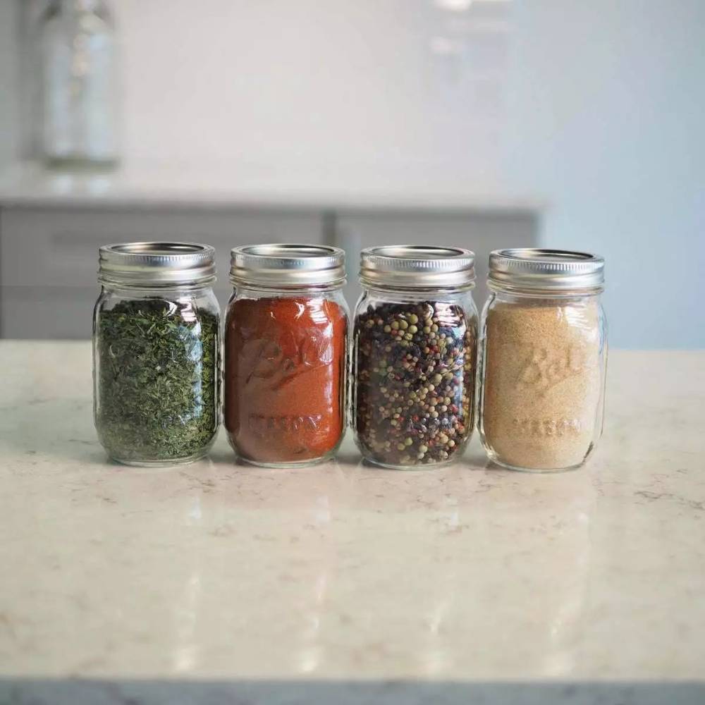 Set of four 4-ounce mini glass storage jars with metal lids, filled with dried herbs, spices, and seasoning, handcrafted in the USA, suitable for Home & Decor and Kitchen & Food collections.