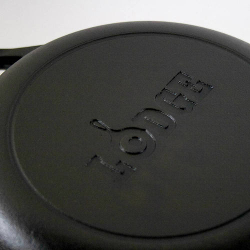Close-up of the bottom of a handcrafted black cast iron skillet embossed with "Lodge," ideal for Kitchen & Food, Cookware, Cast Iron, USA Made, Best Sellers, and Promo Eligible collections.