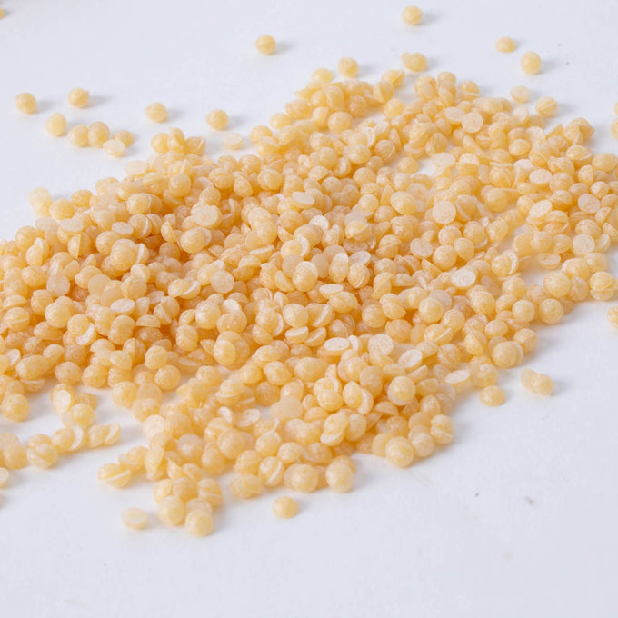 Natural-colored beeswax candle wax pellets scattered on a white surface, handcrafted and ideal for lamps, candlemaking supplies, and best sellers collections.