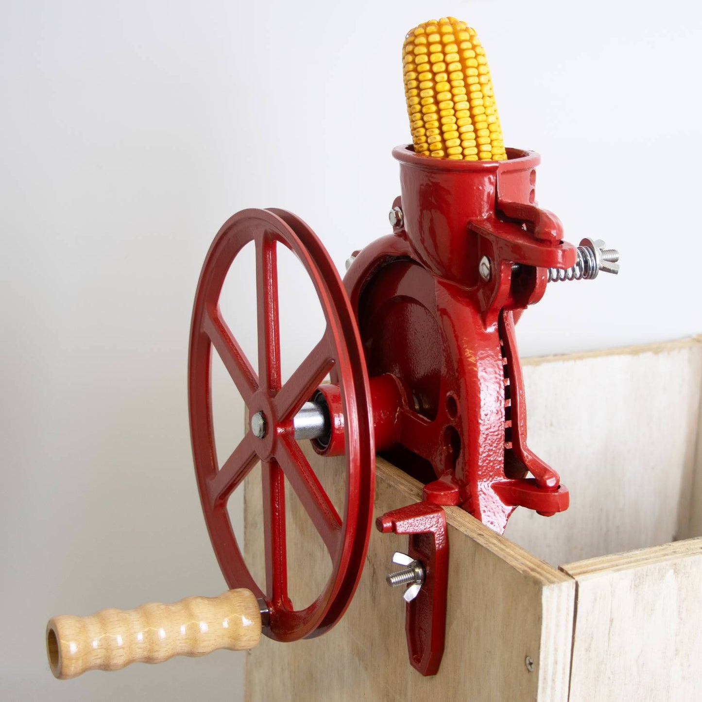 Handcrafted cast iron corn sheller with a red finish and wooden handle clamped to a wooden box, designed for farm, garden, and tool use in farm tools collections.