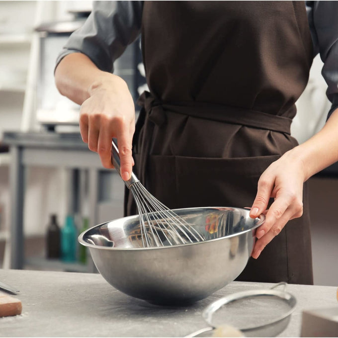 Person wearing a brown apron whisking ingredients in a stainless steel mixing bowl on a kitchen counter, ideal for Kitchen & Food, Baking Supplies, and Cookware collections.