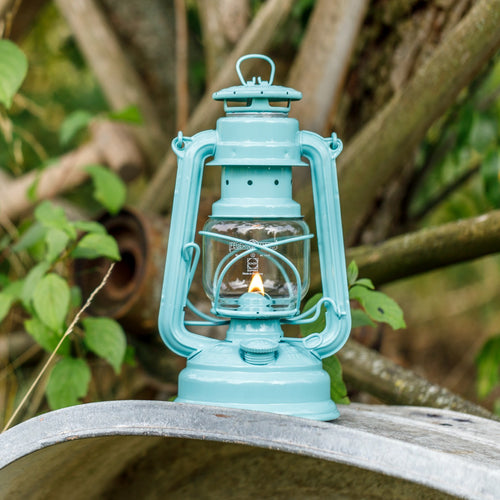 Handcrafted light blue galvanized oil lantern with thermal heat-resistant SUPRAX globe glowing softly outdoors on a metal surface, perfect for Lamps & Lighting, Camping, and Emergency Supplies collections.