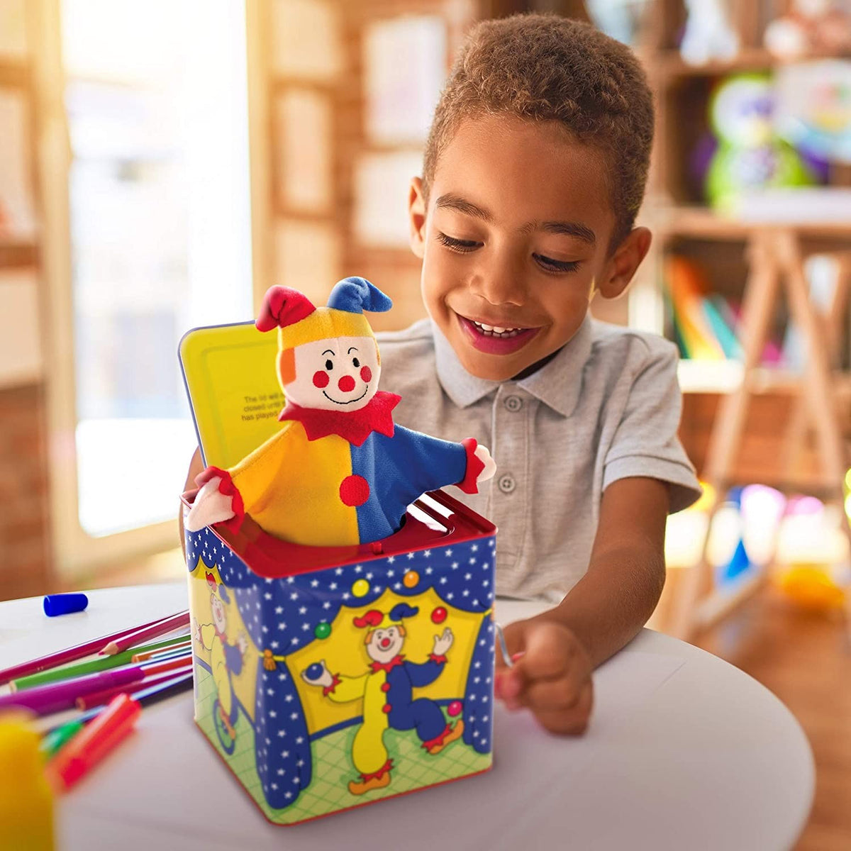 Young boy smiling as he plays with a handcrafted, brightly painted musical jack-in-the-box toy, perfect for indoor play and children’s toy collections.