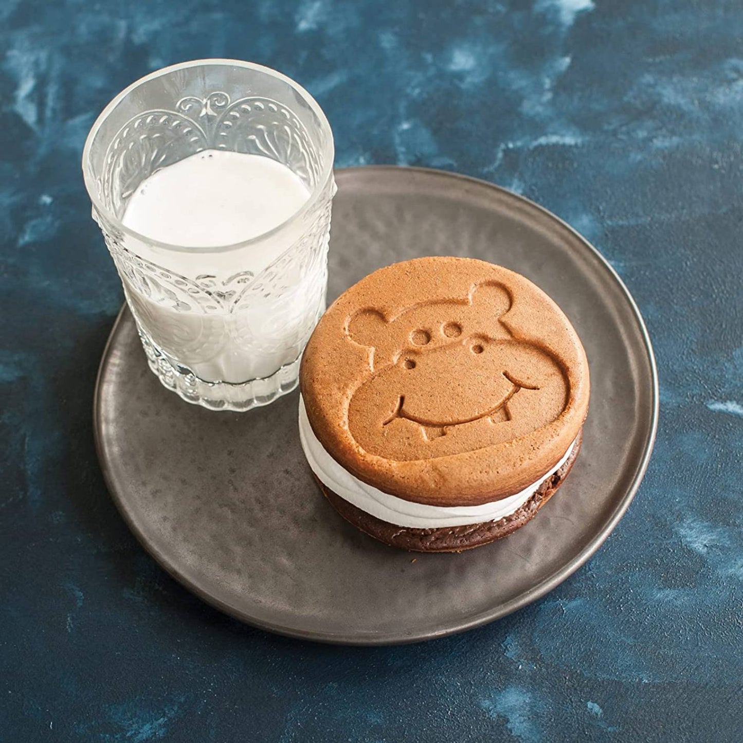 Whimsical animal-shaped pancake sandwich with cream filling on a dark plate next to a glass of milk, showcasing fun breakfast cookware from Kitchen & Food, USA Made collections.