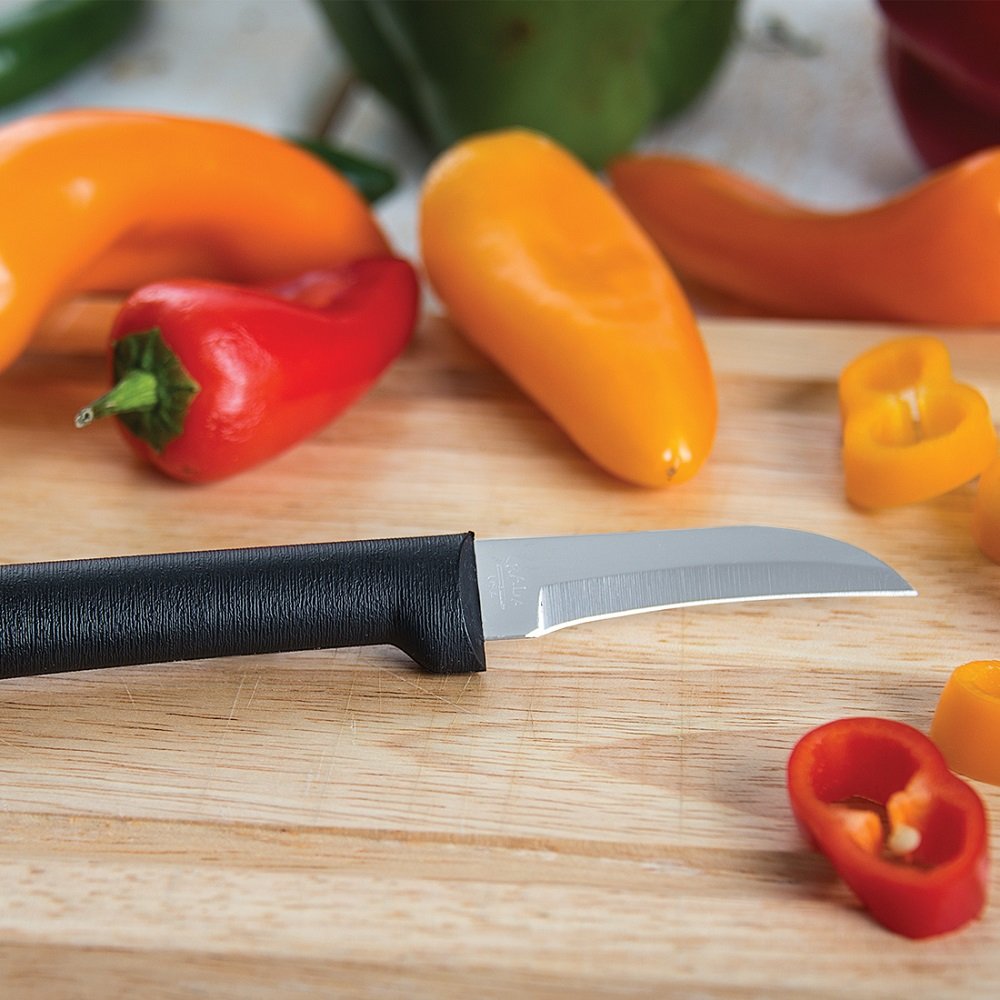 Handcrafted paring knife with a high carbon surgical stainless steel curved blade and black solid handle, resting on a wooden cutting board with sliced red and yellow mini peppers, made in USA, ideal for Farm, Garden & Tool and Kitchen & Food collections.