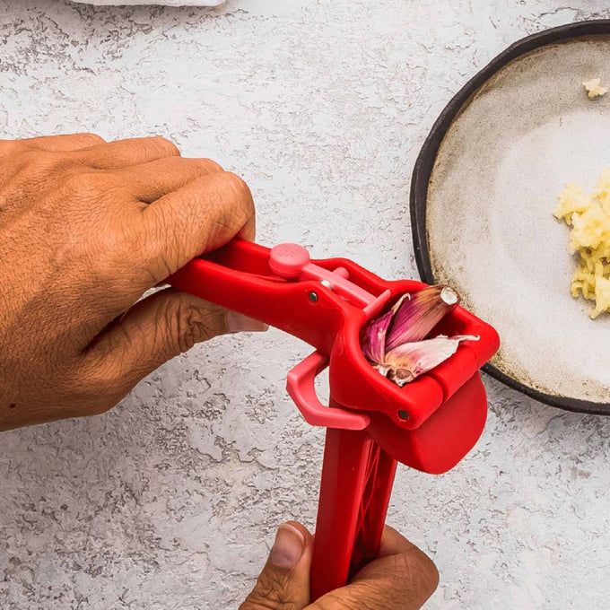 Red garlic press crushing multiple unpeeled cloves with a self-cleaning mechanism that ejects peels, featured in Kitchen & Food, Food Prep, Choppers and Cutters, Kitchen Gadgets, and Best Sellers collections.