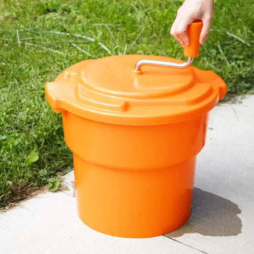 Bright orange handcrafted manual laundry spinner with a crank handle being operated outdoors, designed for faster drying, featured in Home & Decor and Laundry Supplies collections.