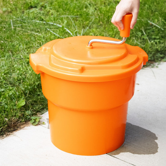 Bright orange handcrafted manual laundry spinner with a crank handle being operated outdoors, designed for faster drying, featured in Home & Decor and Laundry Supplies collections.