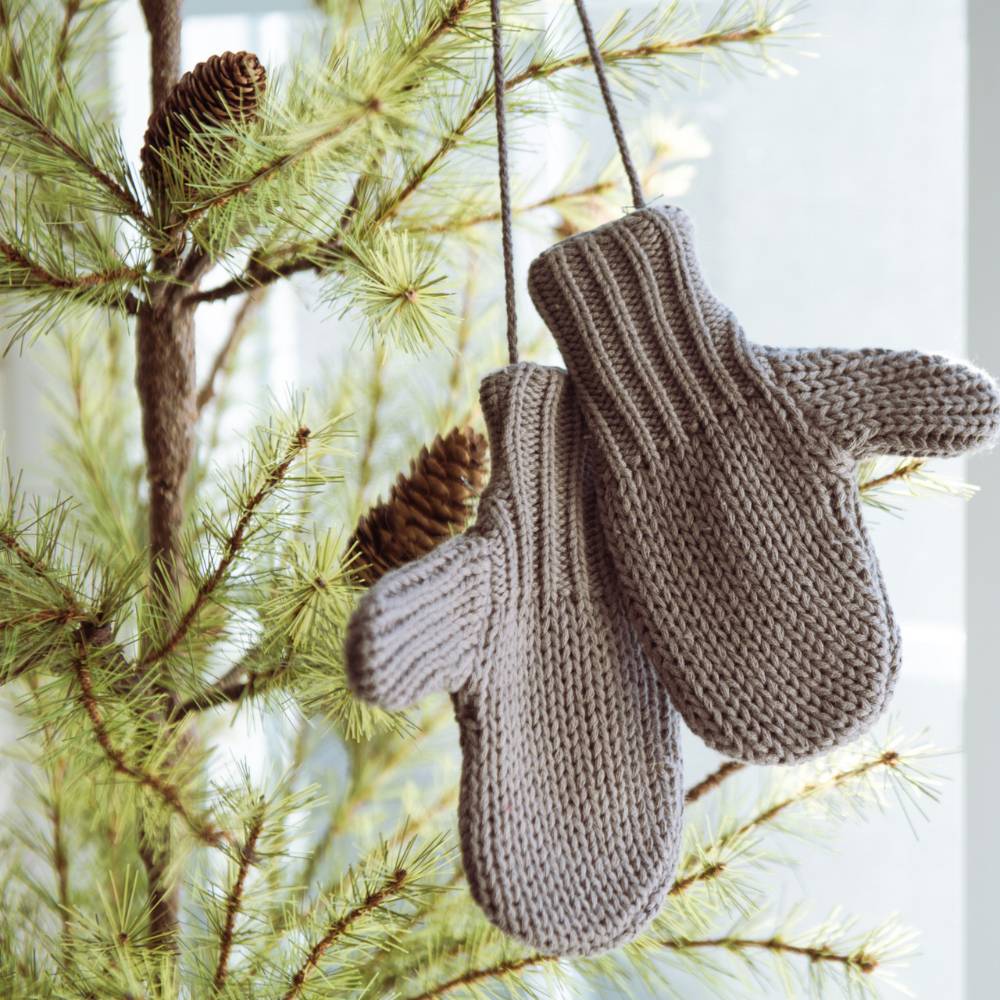 Pair of gray cotton blend mittens hanging on a pine tree branch, adding a cozy touch to holiday decor, featured in Home & Decor and Holiday Decor collections.