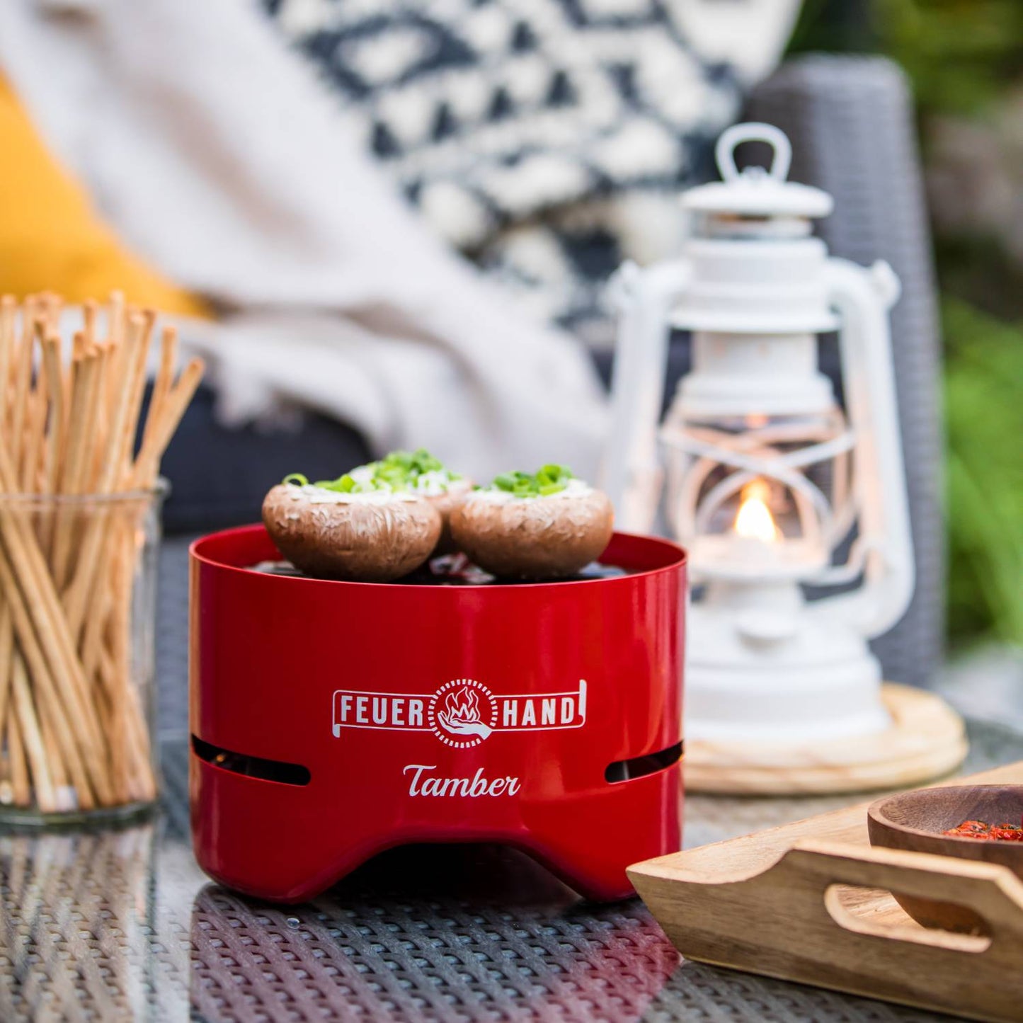 Handcrafted red tabletop charcoal grill with two stuffed mushrooms cooking over low heat, set on a metal patio table with a white vintage lantern and wooden tray, ideal for Farm, Garden & Tool, Camping, and Grilling collections.