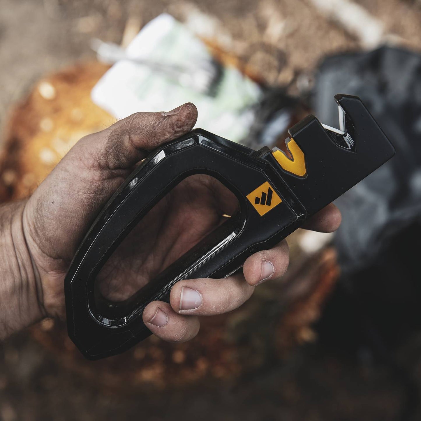 Handheld black knife and tool sharpener with ergonomic handle and yellow sharpening guide, shown in use outdoors, ideal for Farm, Garden & Tool, Hand Tools and Hardware collections.