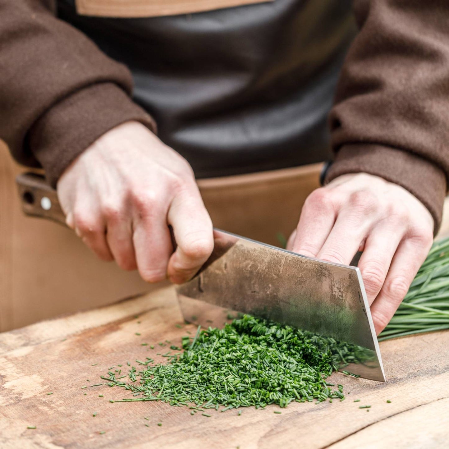 Handcrafted cleaver knife with a sturdy blade chopping fresh green herbs on a wooden surface, perfect for food preparation in kitchen, camping, and butchering tool collections.