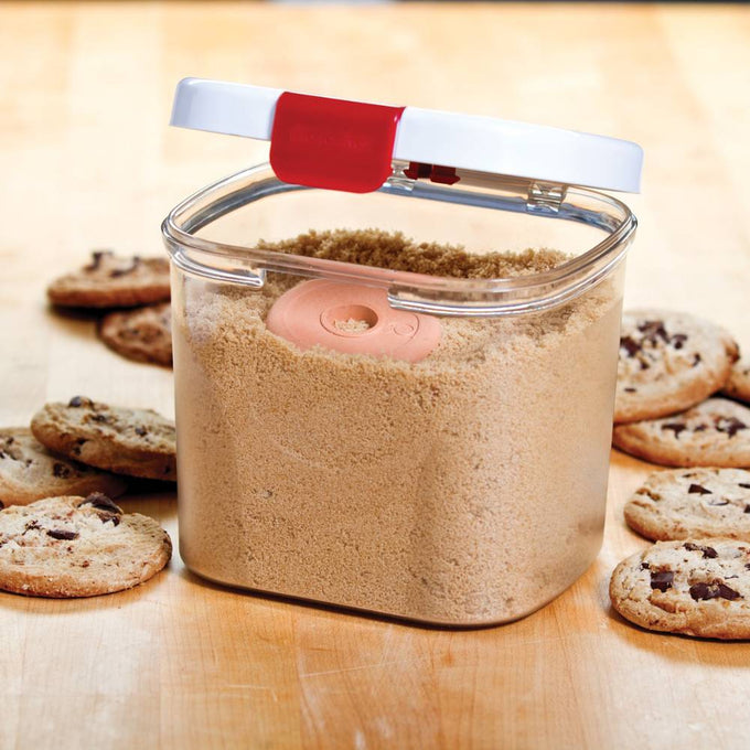 Clear plastic storage container with snap-shut white lid and red clasp, holding brown sugar with a terra cotta moisture-absorbing piece inside, surrounded by chocolate chip cookies, ideal for Kitchen & Food and Storage and Serving collections.