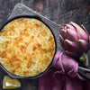 Baked creamy artichoke dip with golden melted cheese in an 8-inch cast iron skillet, styled with fresh artichoke, lemon wedge, and purple cloth, perfect for Kitchen & Food, Dry Goods and Mixes, Best Sellers, Promo Eligible collections.