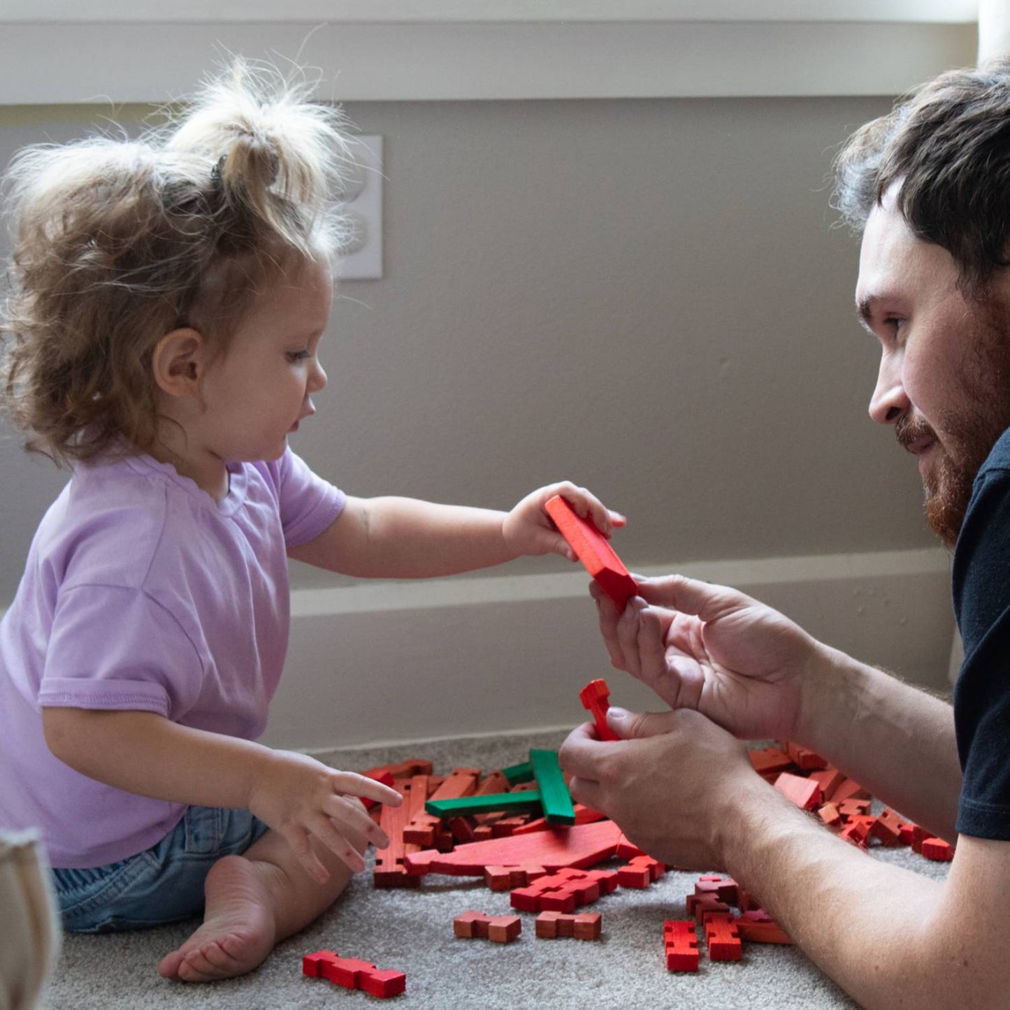 Young child and adult playing together with handcrafted wooden log pieces in red and green, promoting imaginative indoor play and part of USA Made and Toys, Books & Games collections.