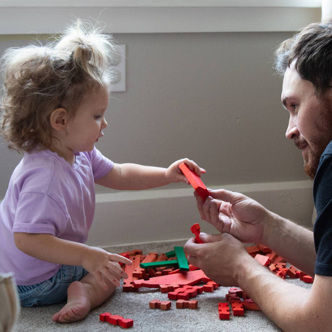 Young child and adult playing together with handcrafted wooden log pieces in red and green, promoting imaginative indoor play and part of USA Made and Toys, Books & Games collections.