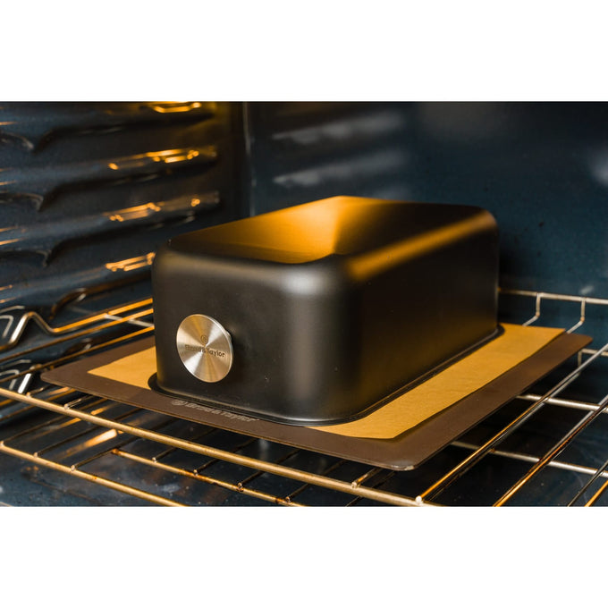 Lightweight black baking shell with smooth edges and a metal logo medallion, placed on a baking tray inside an oven, ideal for Kitchen & Food, Cookware, Baking Supplies, and Bread Making collections.