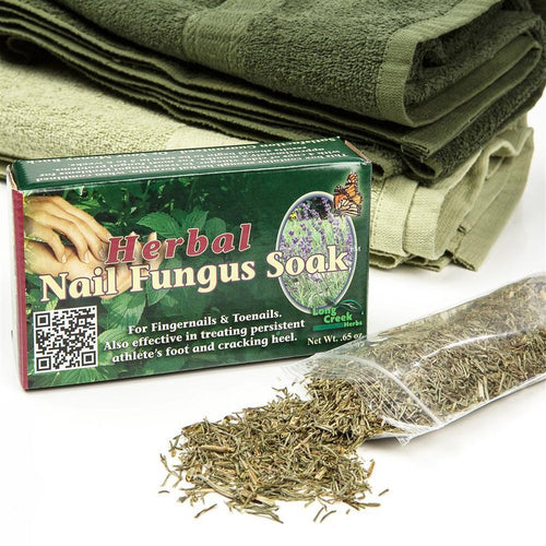 Box of herbal nail fungus soak with loose dried herbs spilling from clear plastic bag, placed in front of folded green towels, highlighting a natural health remedy in USA Made and Health & Wellness collections.