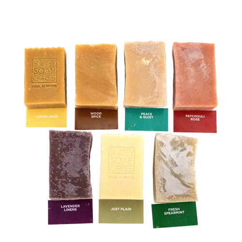 Seven handcrafted natural soap bars in assorted colors and scents, each labeled with names and packaging tags, featured in Health & Wellness, Soaps and Soapmaking, USA Made, and Best Sellers collections.