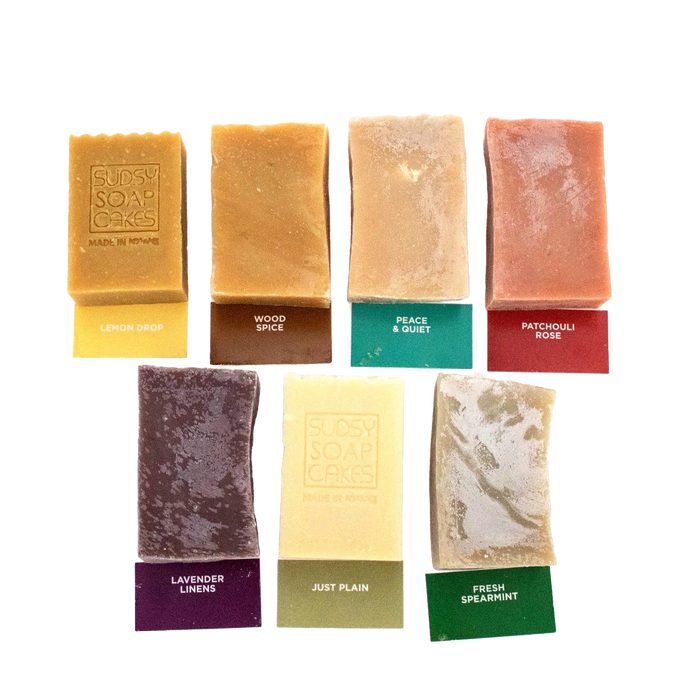 Seven handcrafted natural soap bars in assorted colors and scents, each labeled with names and packaging tags, featured in Health & Wellness, Soaps and Soapmaking, USA Made, and Best Sellers collections.