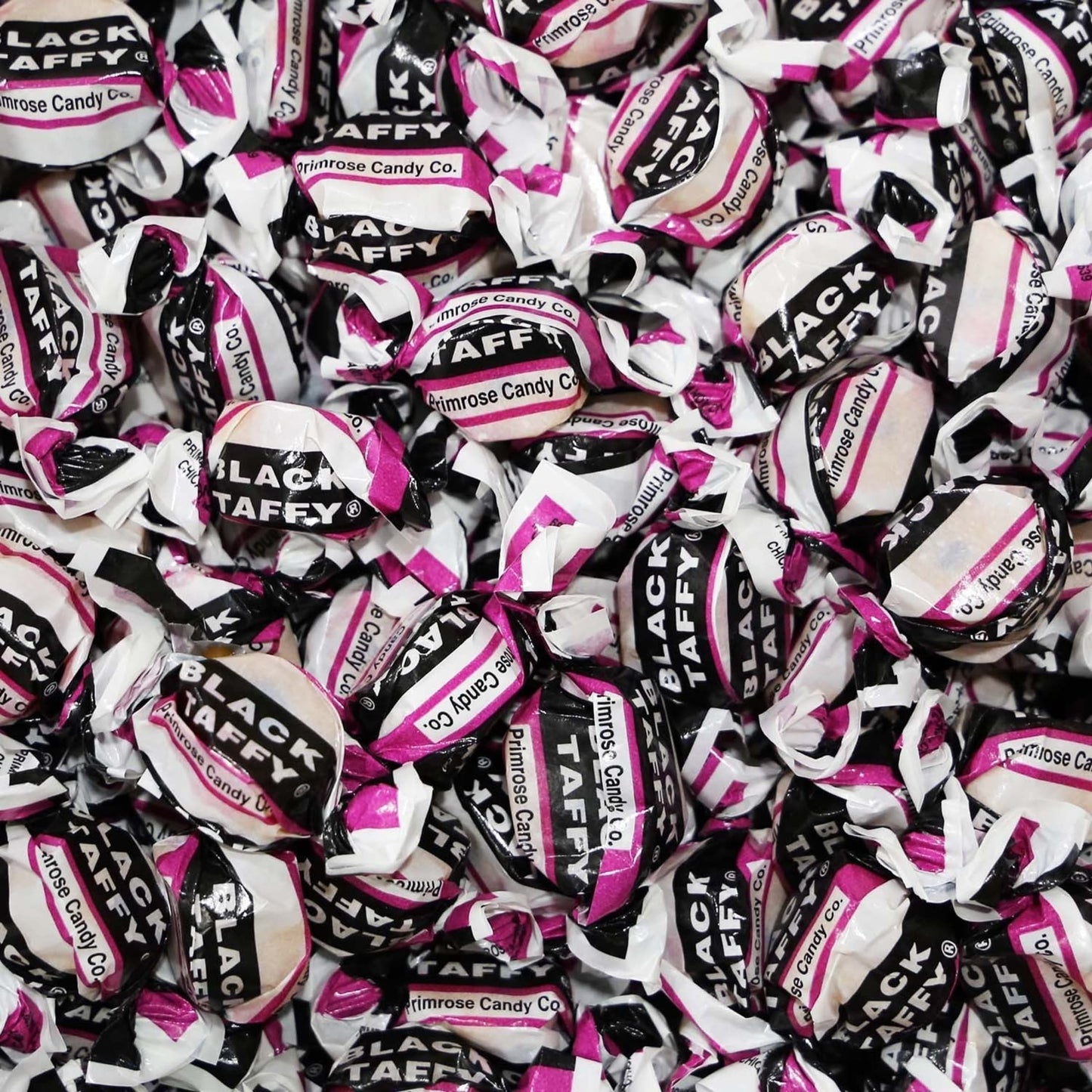 Close-up of individually wrapped black taffy candies in white, black, and purple packaging, representing handcrafted nostalgic sweets from Kitchen & Food, Snacks and Sweets, Best Sellers, and Promo Eligible collections.