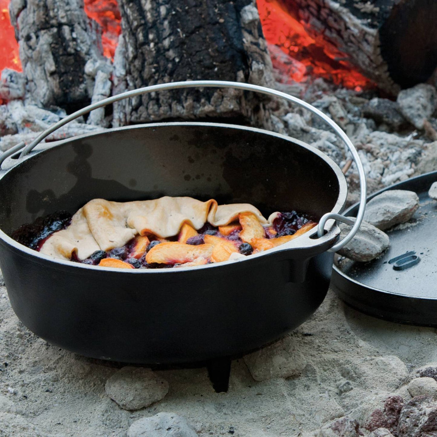 Handcrafted cast iron camp Dutch oven with built-in legs baking a rustic fruit dessert by an open campfire; ideal for Farm, Garden & Tool, Camping, Cast Iron, USA Made, Best Sellers, and Promo Eligible collections.